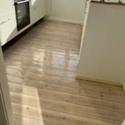 Køkken med nylakeret lyst trægulv og moderne hvide skabe.